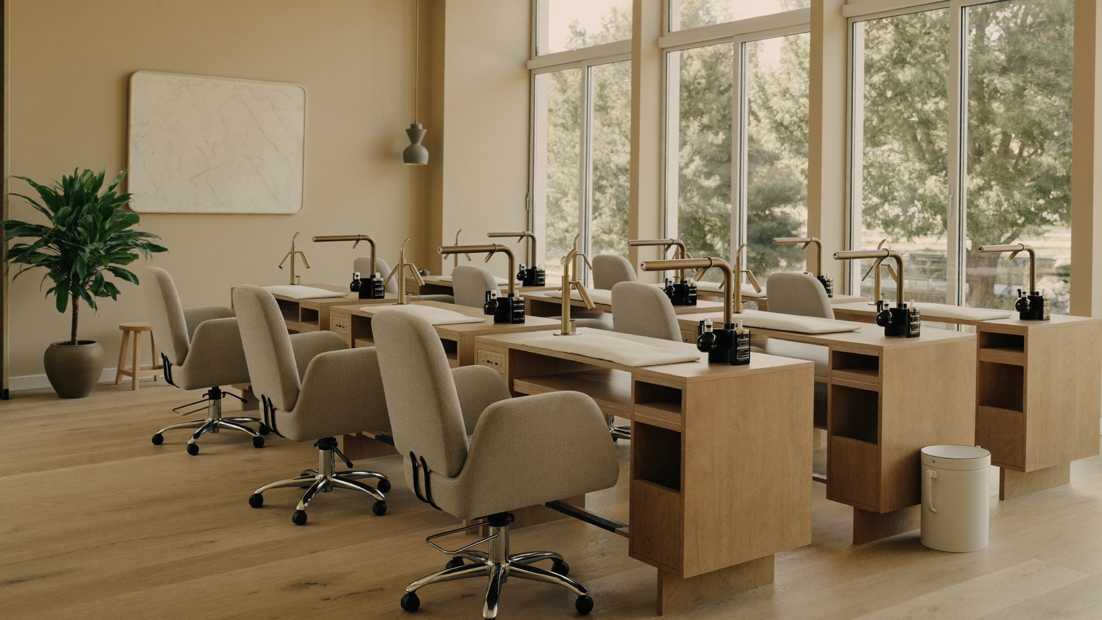 Interior of a bright, modern nail salon with pale oak stations and large windows.